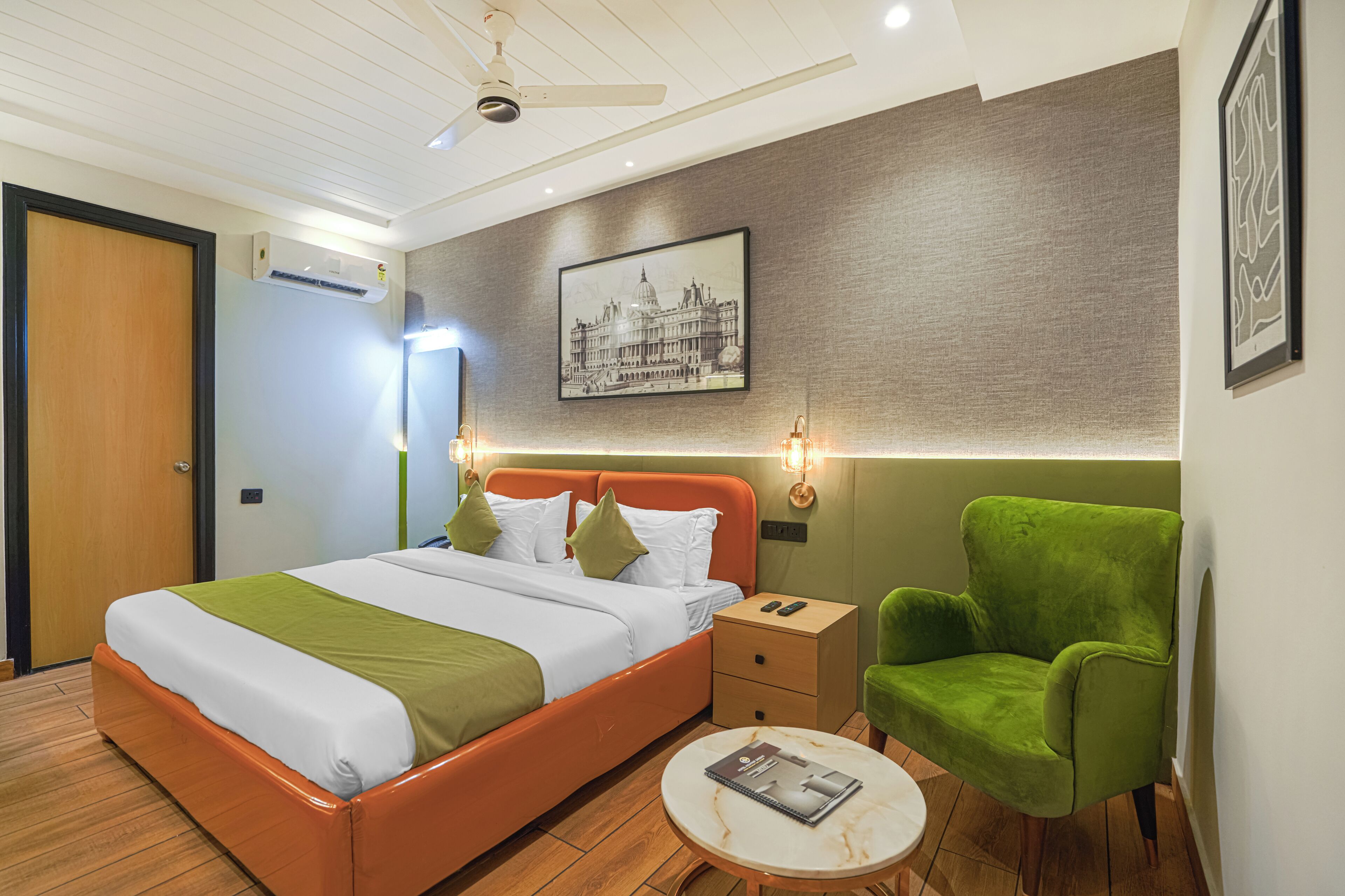 A hotel room with a bed, bedside table, green chair, and a round table.
