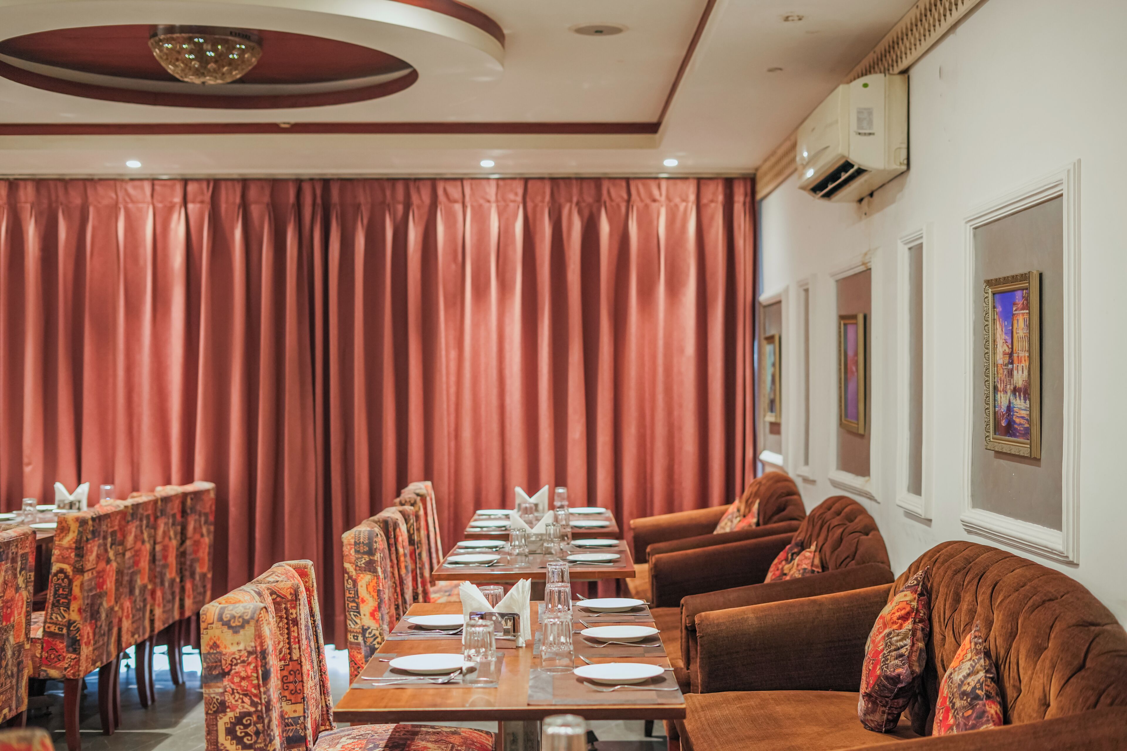 A dining area with a long table set for a meal, surrounded by patterned chairs and sofas.