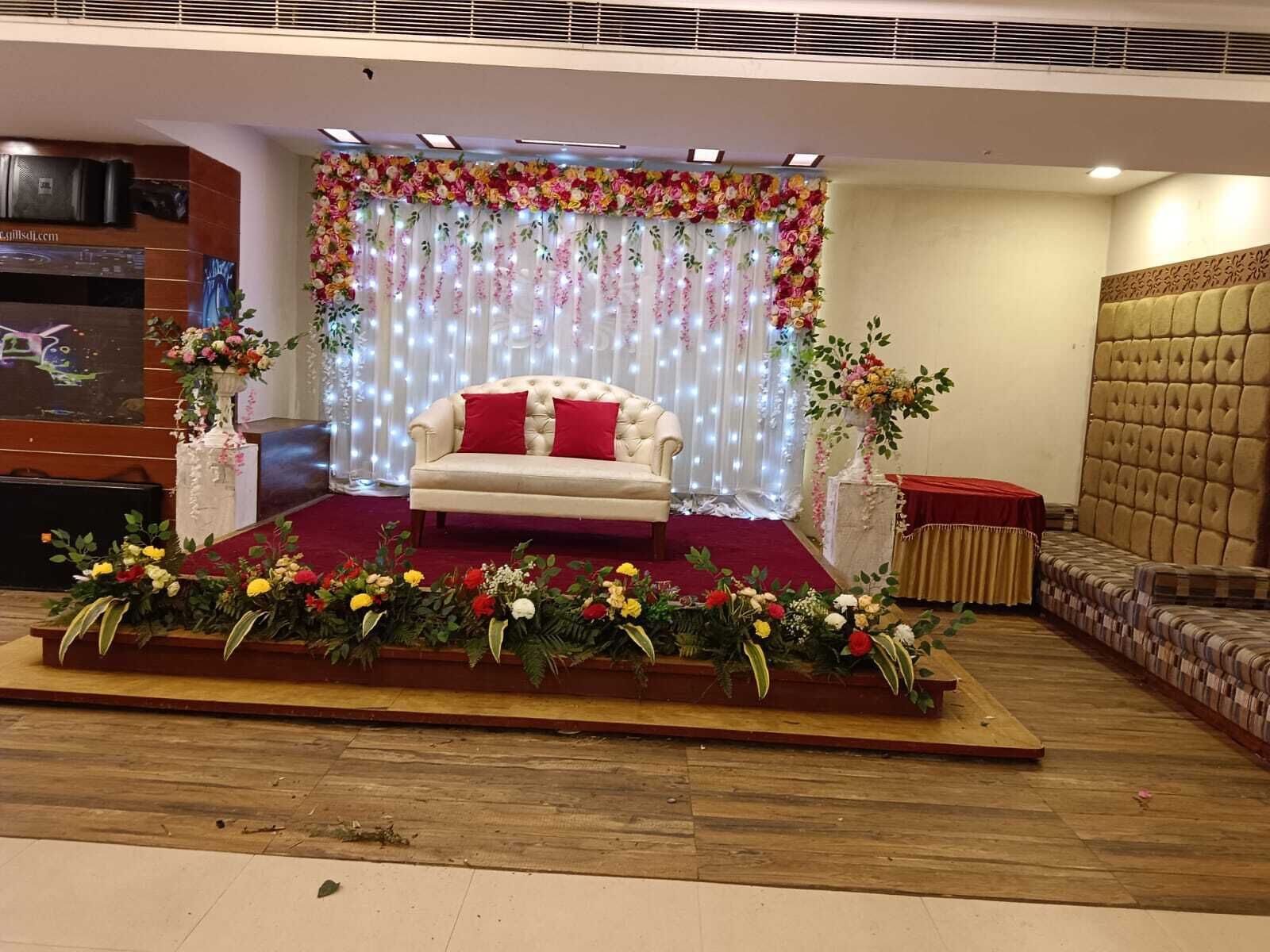Un escenario con un sofá blanco y cojines rojos, rodeado de arreglos florales y cubierto con un cortinaje floral.