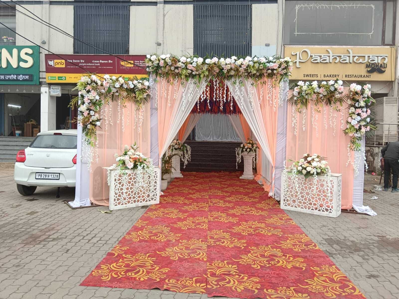 A decorated entrance with a red carpet leading to a staircase, surrounded by floral arrangements and draped fabric.