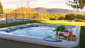 Un bain à remous doté d’une terrasse en bois, entouré d’une clôture, et offrant une vue panoramique sur des collines et des arbres en arrière-plan.