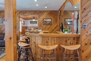 A rustic wooden interior with a bar area featuring wooden stools and a counter. - Mountainview Estate | Private Lake + Heated Pool, Spa + Game Room | 12BR Retreat (Hensonville)
