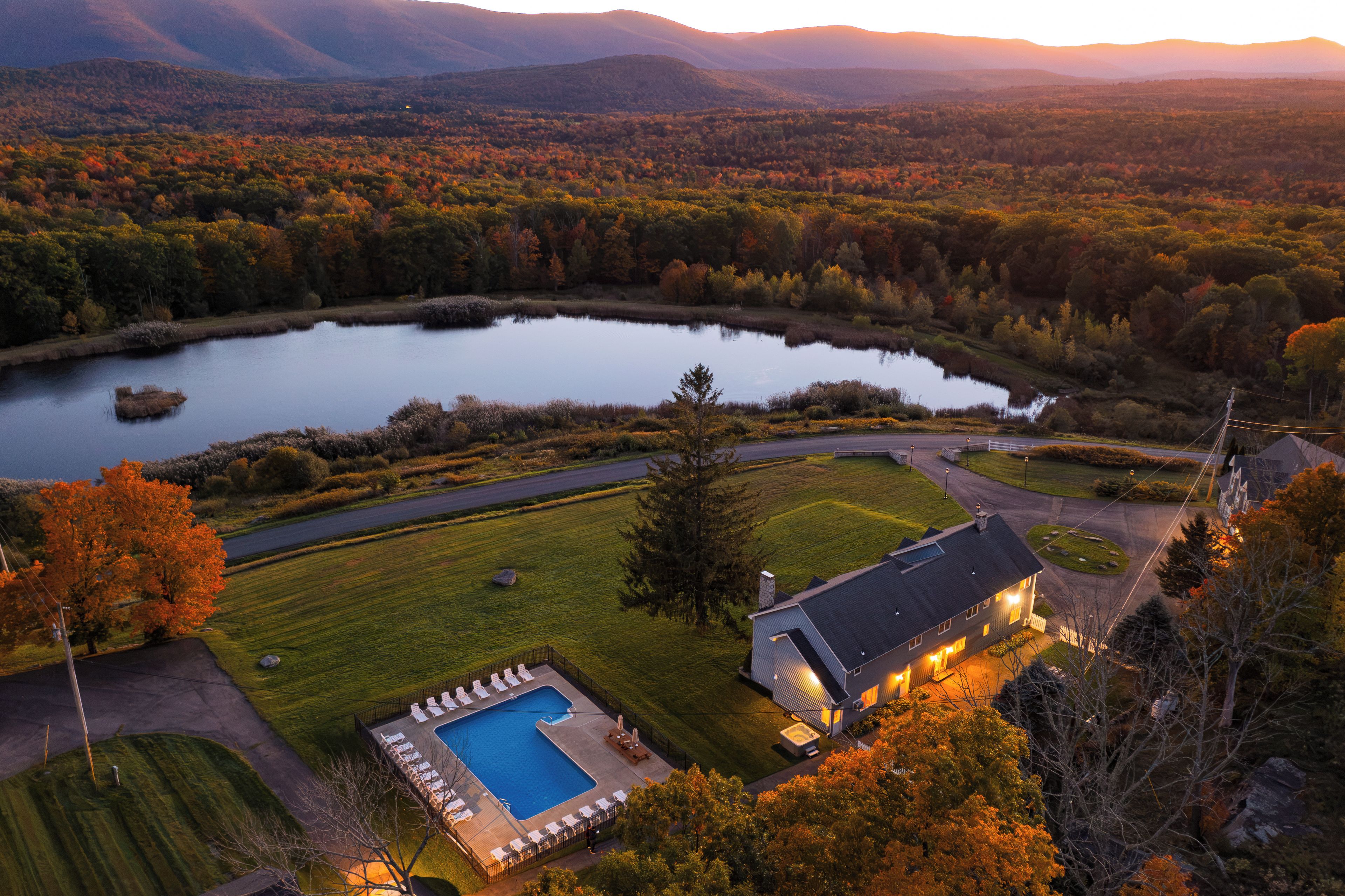 Un lago grande rodeado de árboles, una piscina y una casa con un césped cuidado.