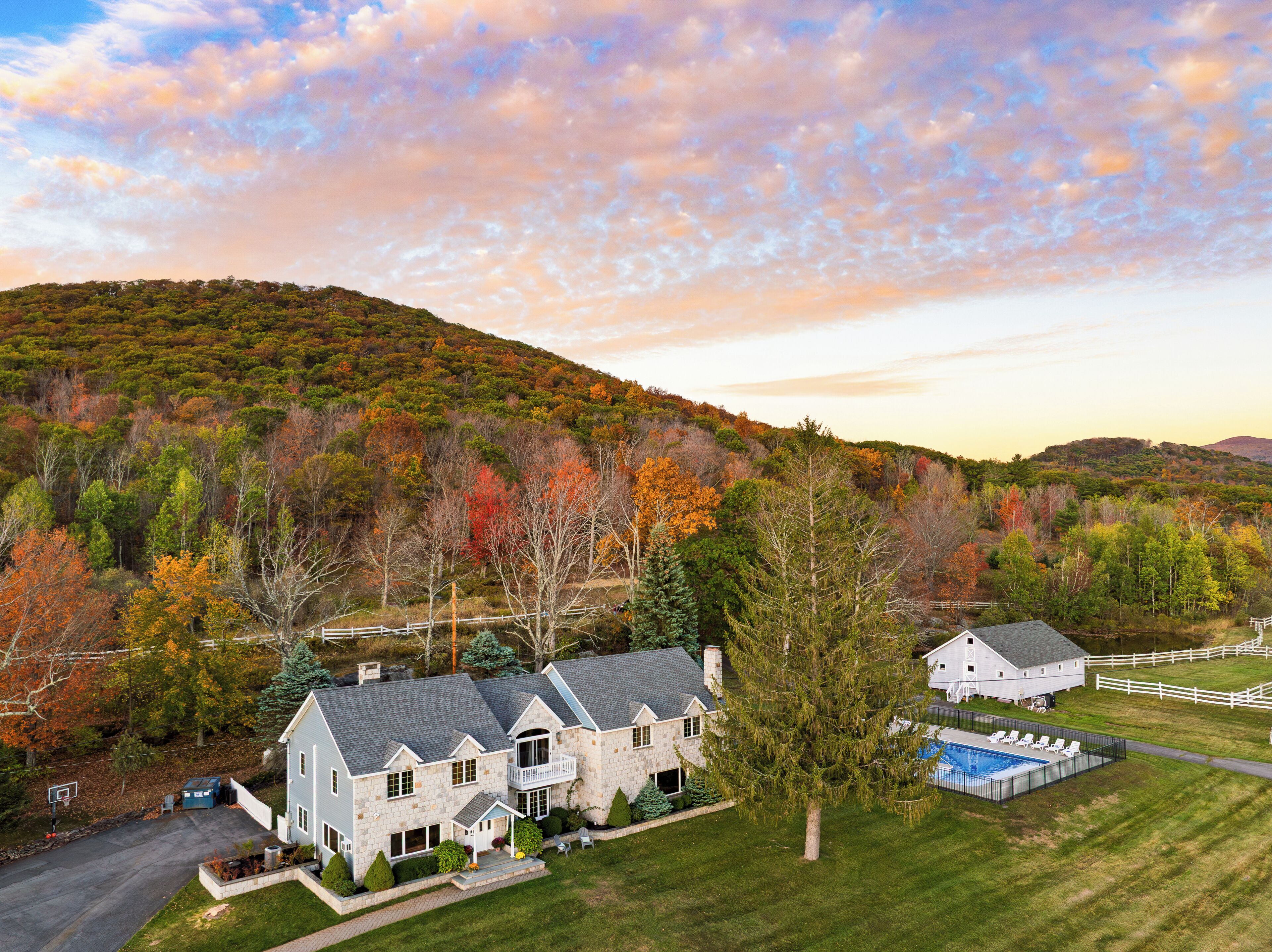 Une grande maison en pierre dotée d’une piscine, entourée d’une cour clôturée et d’arbres aux couleurs automnales.