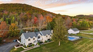 Une grande maison en pierre dotée d’une piscine, entourée d’une cour clôturée et d’arbres aux couleurs automnales.