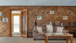 Un salón acogedor con una pared de madera en espiga, un sofá de cuero marrón, una mesa de centro de madera con piezas de ajedrez y una puerta que da al exterior.