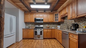 Una cocina con armarios de madera, un refrigerador de acero inoxidable, un microondas, un horno y una salpicadura trasera de azulejos.