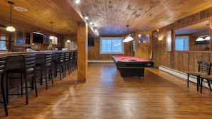 Un interior de madera con mesa de billar, zona de bar y asientos.