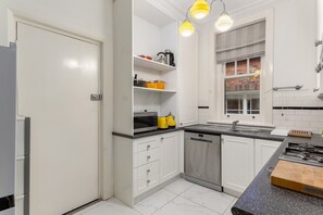 A modern kitchen with white cabinets, a stainless steel dishwasher, a granite countertop, and a window with a view of a brick building. - Eclectic Art Deco Apartment in great location (Potts Point)