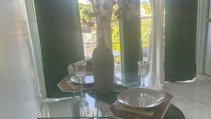 Ein Essbereich mit einem Glastisch, gedeckt für zwei Personen, einer Blumenvase und Blick auf Grünfläche.