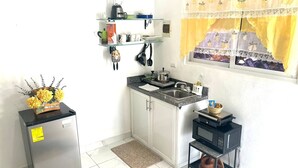 Eine kompakte Küche mit Kühlschrank, Mikrowelle und Herd. Über der Arbeitsfläche befinden sich Regale mit verschiedenen Küchenutensilien.