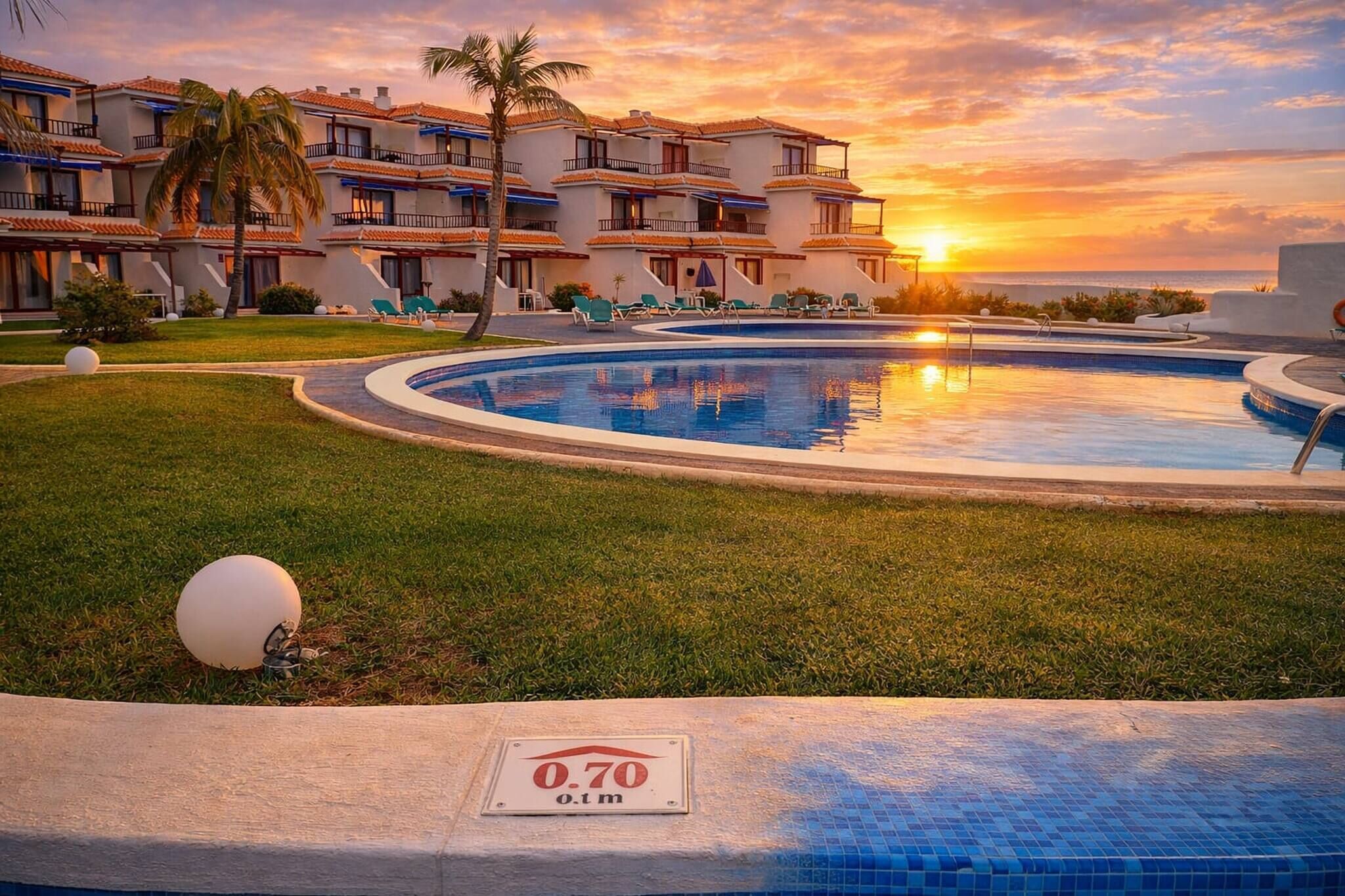 A hotel with a swimming pool, palm trees, and a sunset view.