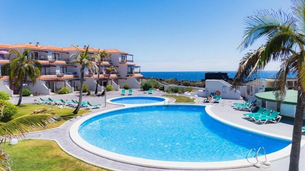 Een resort met een groot zwembad, ligbedden en uitzicht op de oceaan.