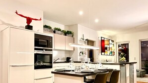 A modern kitchen with white cabinetry, a central island with chairs, and a red sculpture on top. - Penthouse with XL terrace | including parking space | top connection to the old town (Nürnberg)