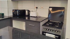 A modern kitchen with grey cabinets, a black countertop, a stove, a toaster, and a kettle. - Private Stylish Flat in Nyali Mombasa with Pool near Beach (Mombasa)