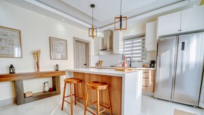 Uma cozinha moderna com uma ilha central, banquetas de bar, eletrodomésticos de aço inoxidável e obras de arte decorativas nas paredes.