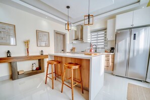 A modern kitchen with a central island, bar stools, stainless steel appliances, and decorative wall art. - A winter get away to SunCity Village (Punta Cana)