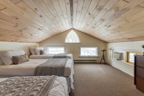 Une chambre avec un plafond en pente, deux lits, une fenêtre, un radiateur et une commode.