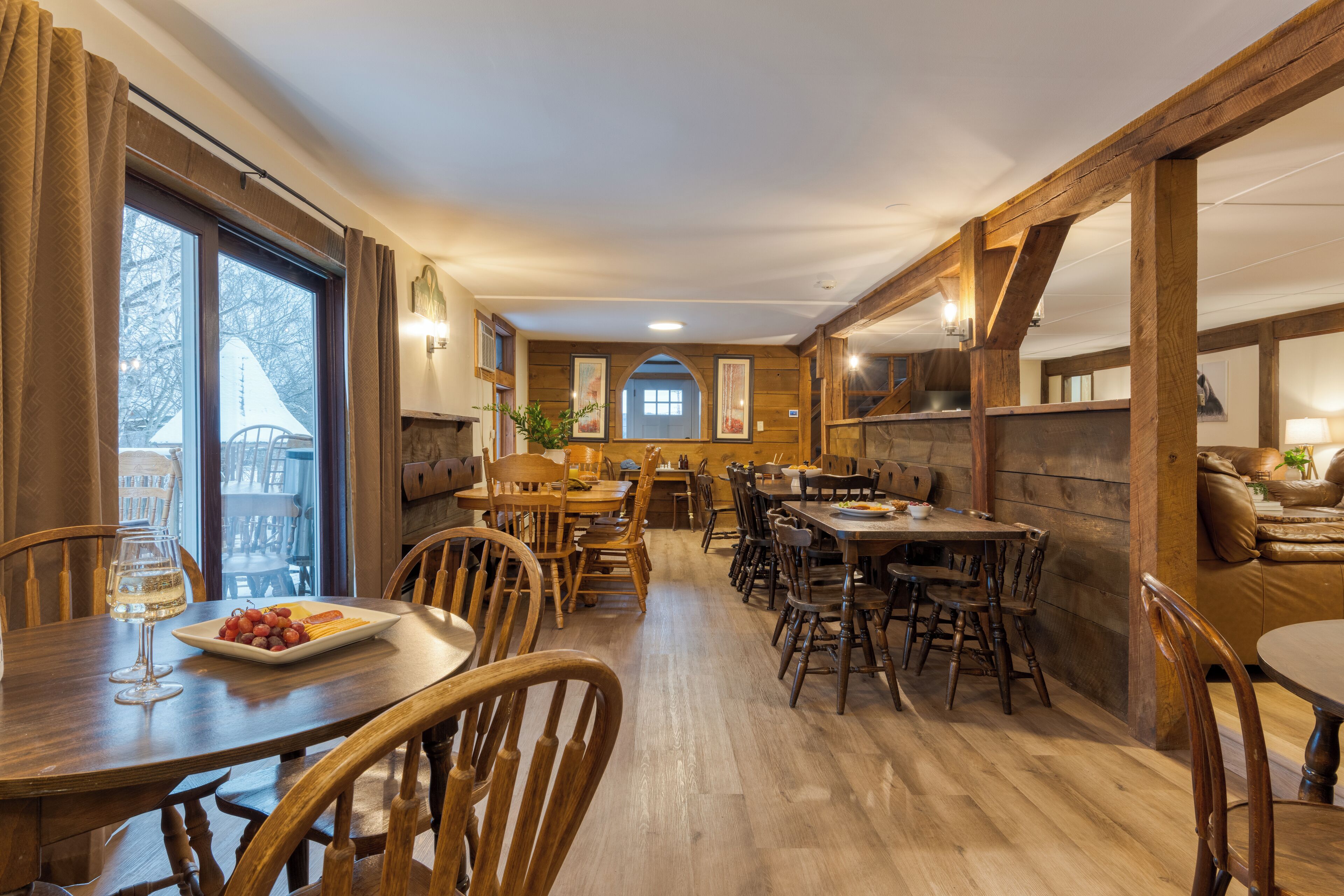 Un vaste espace dédié à la salle à manger, avec des tables et des chaises en bois, une grande fenêtre agrémentée de rideaux et une vue sur l’extérieur.