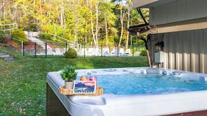 Ein Whirlpool mit Buch und Kerzen, umgeben von einem Zaun und Bäumen.