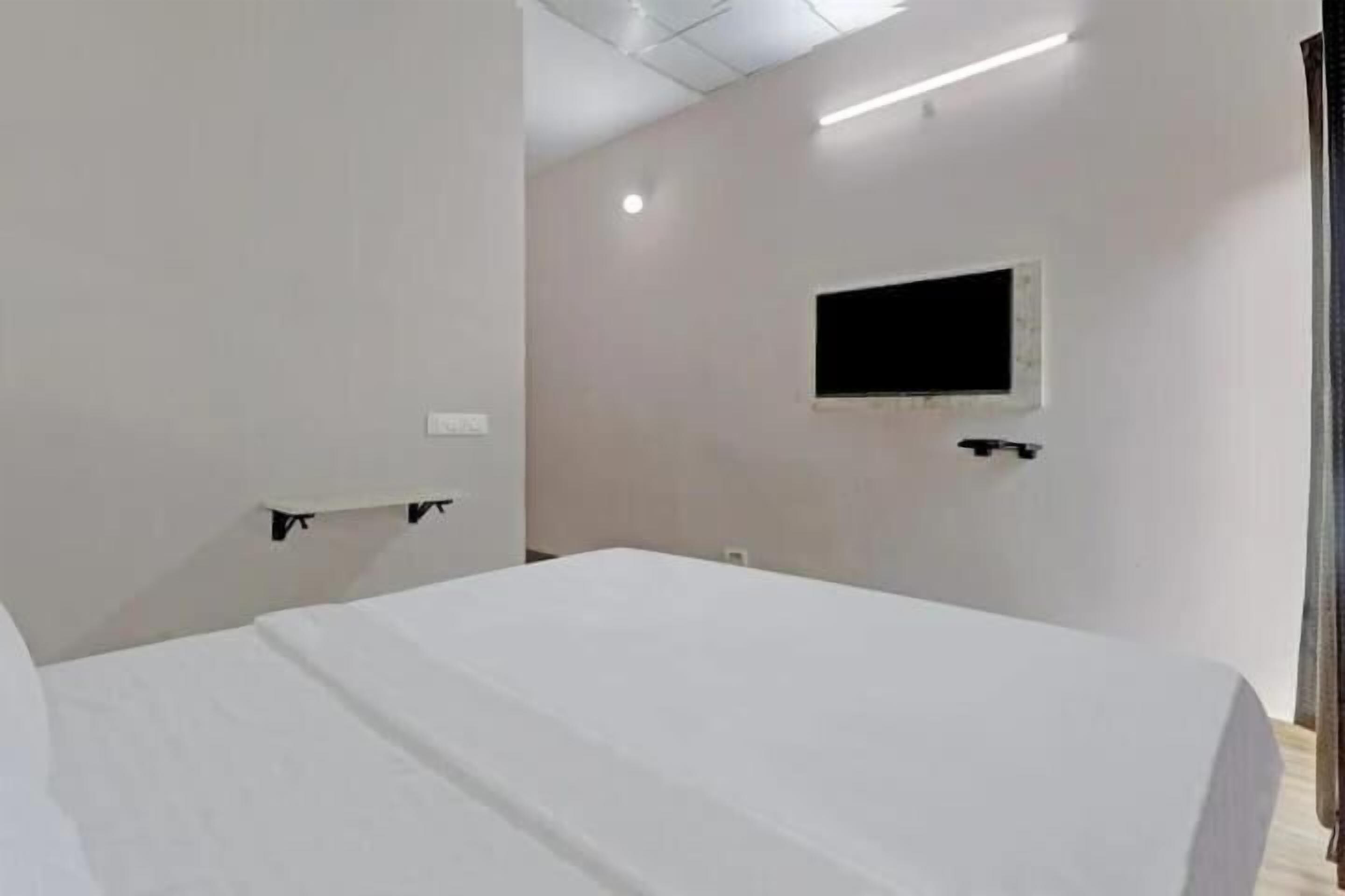 A hotel room with a bed, a small window, and a wall-mounted TV.