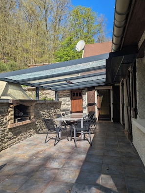 A stone patio with a glass table and chairs, a stone fireplace, and a covered outdoor area with a door.
