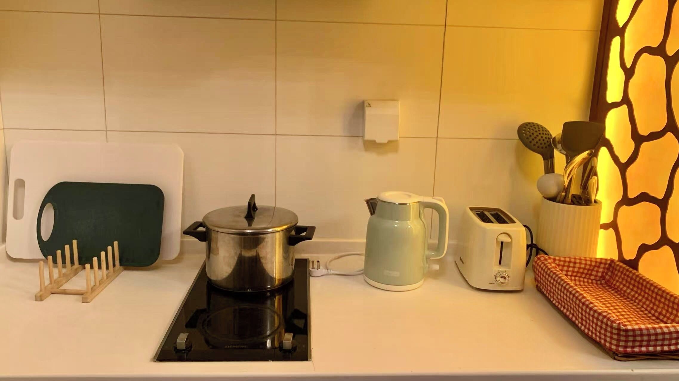 Una cocina con estufa, olla, hervidor, tostadora y utensilios sobre la encimera.