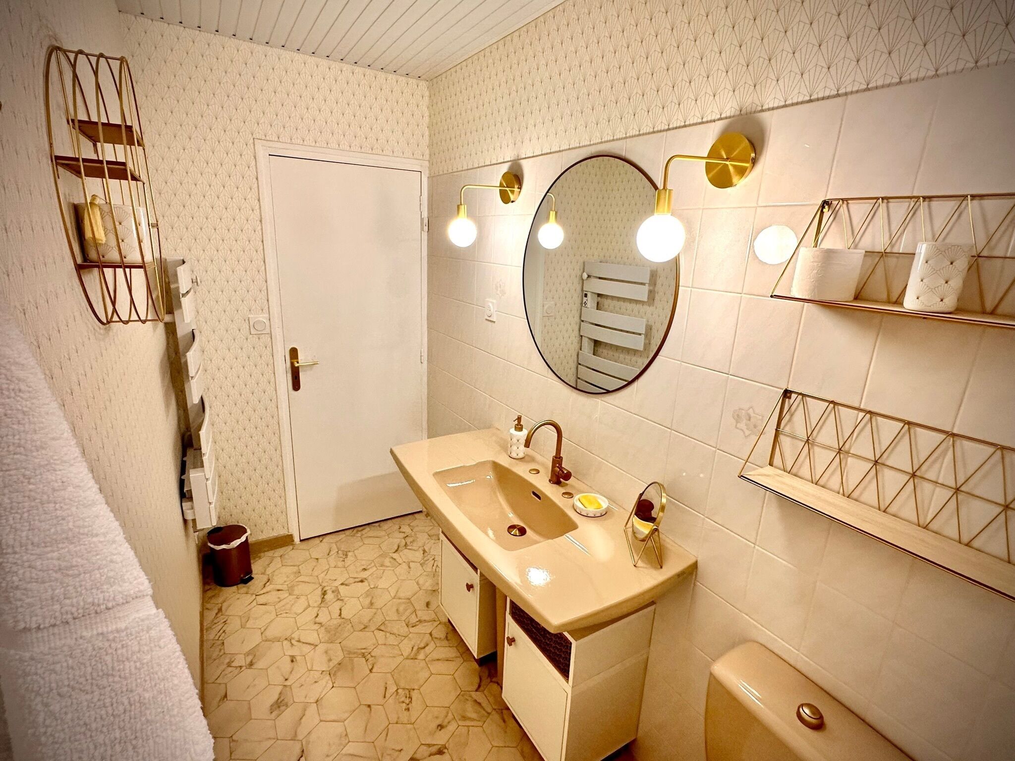 A bathroom with a white door, a sink with a mirror above it, and a toilet. There are three wall-mounted lights above the mirror.