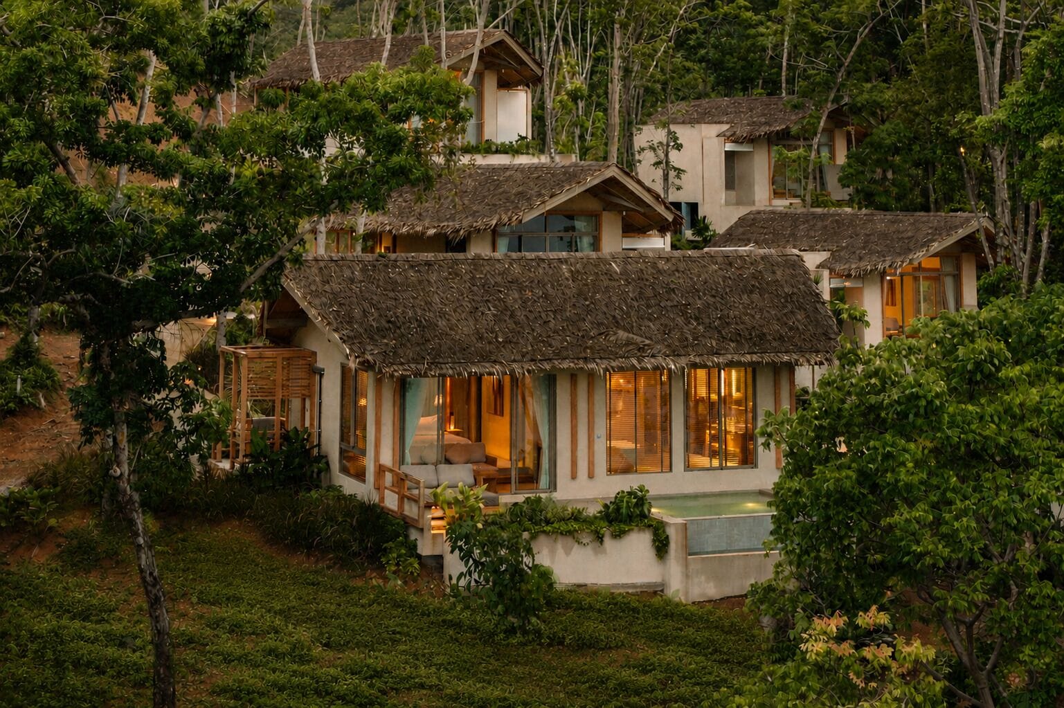 A bungalow with a thatched roof, surrounded by lush greenery.