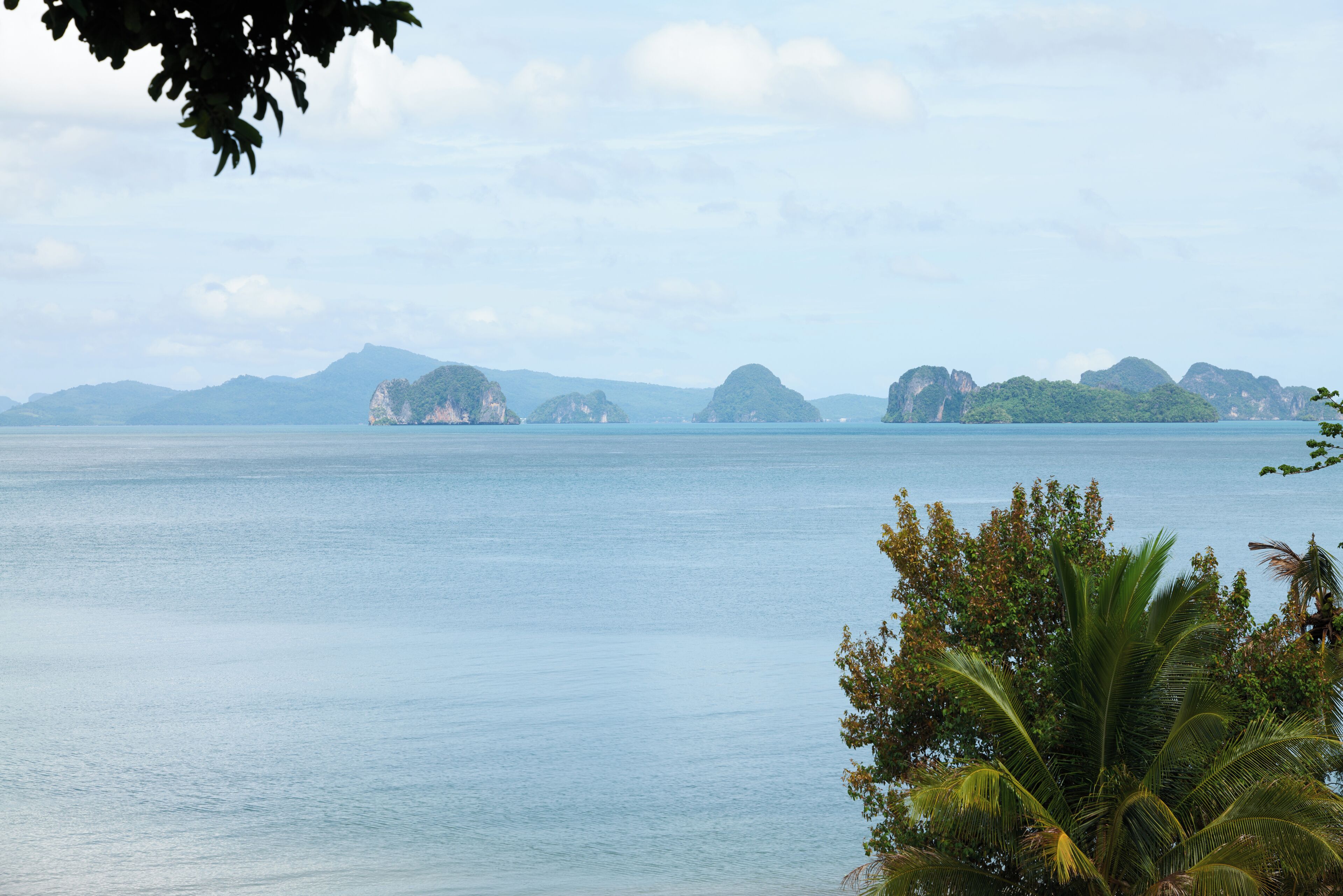 A coastal view with calm water, distant islands, and a palm tree in the foreground.