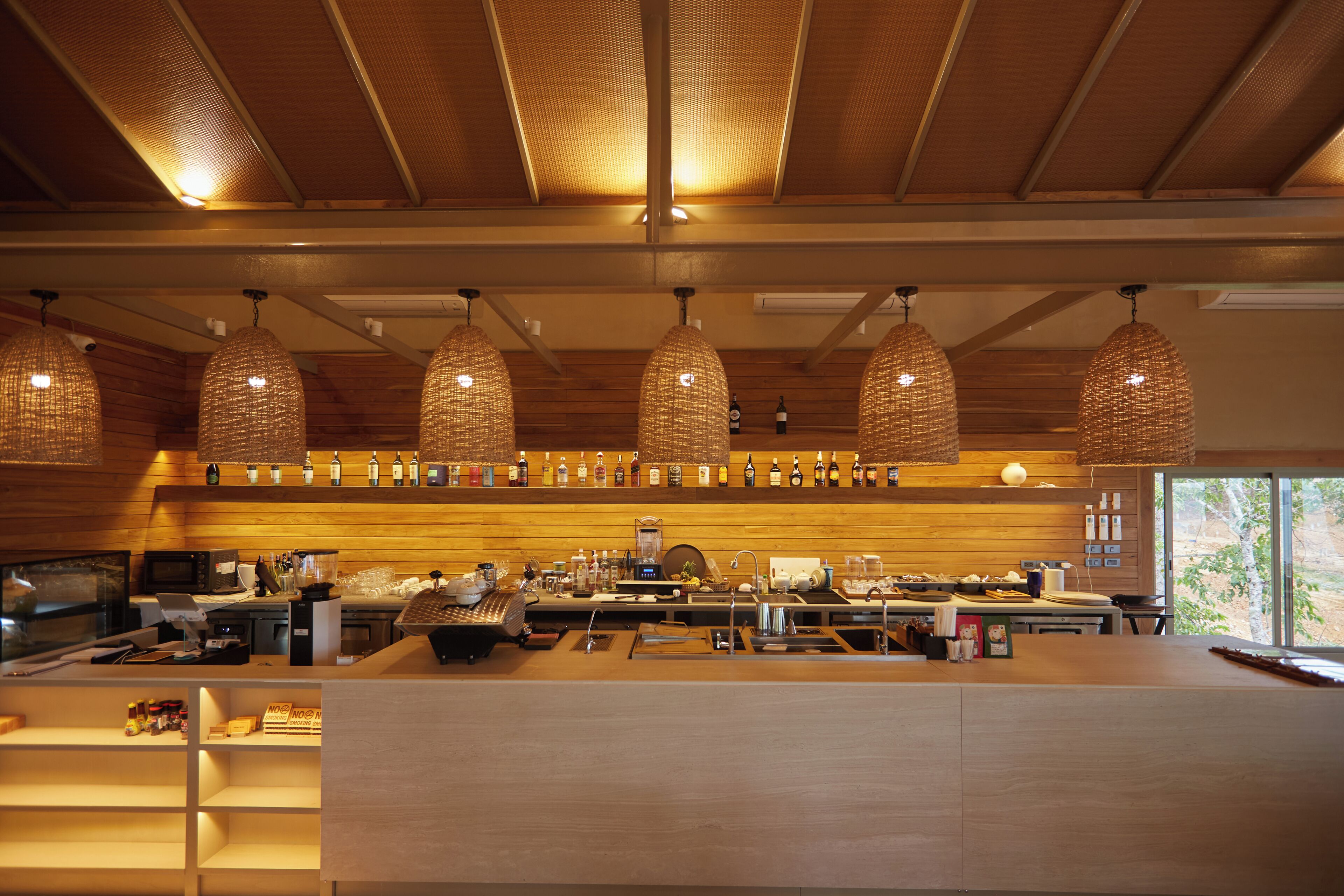 A bar area with hanging wicker chandeliers, wooden walls, and a variety of bottles on shelves.