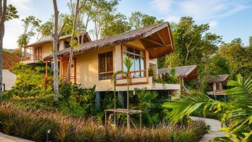 A two-story building with a thatched roof, surrounded by lush greenery and a paved walkway.