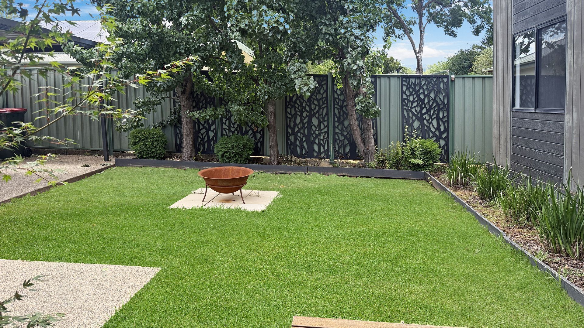 A backyard with a well-maintained lawn, a metal fire pit, and a decorative fence.