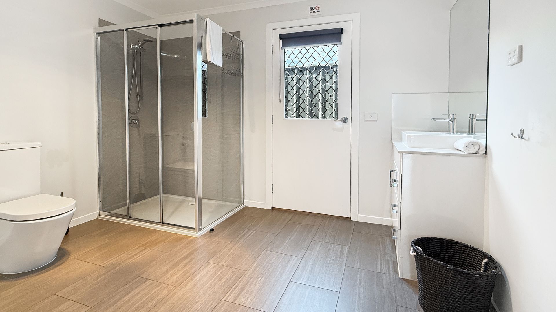A bathroom with a glass-enclosed shower, a toilet, a sink, and a trash bin.