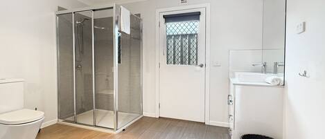 A bathroom with a glass-enclosed shower, a toilet, a sink, and a trash bin.