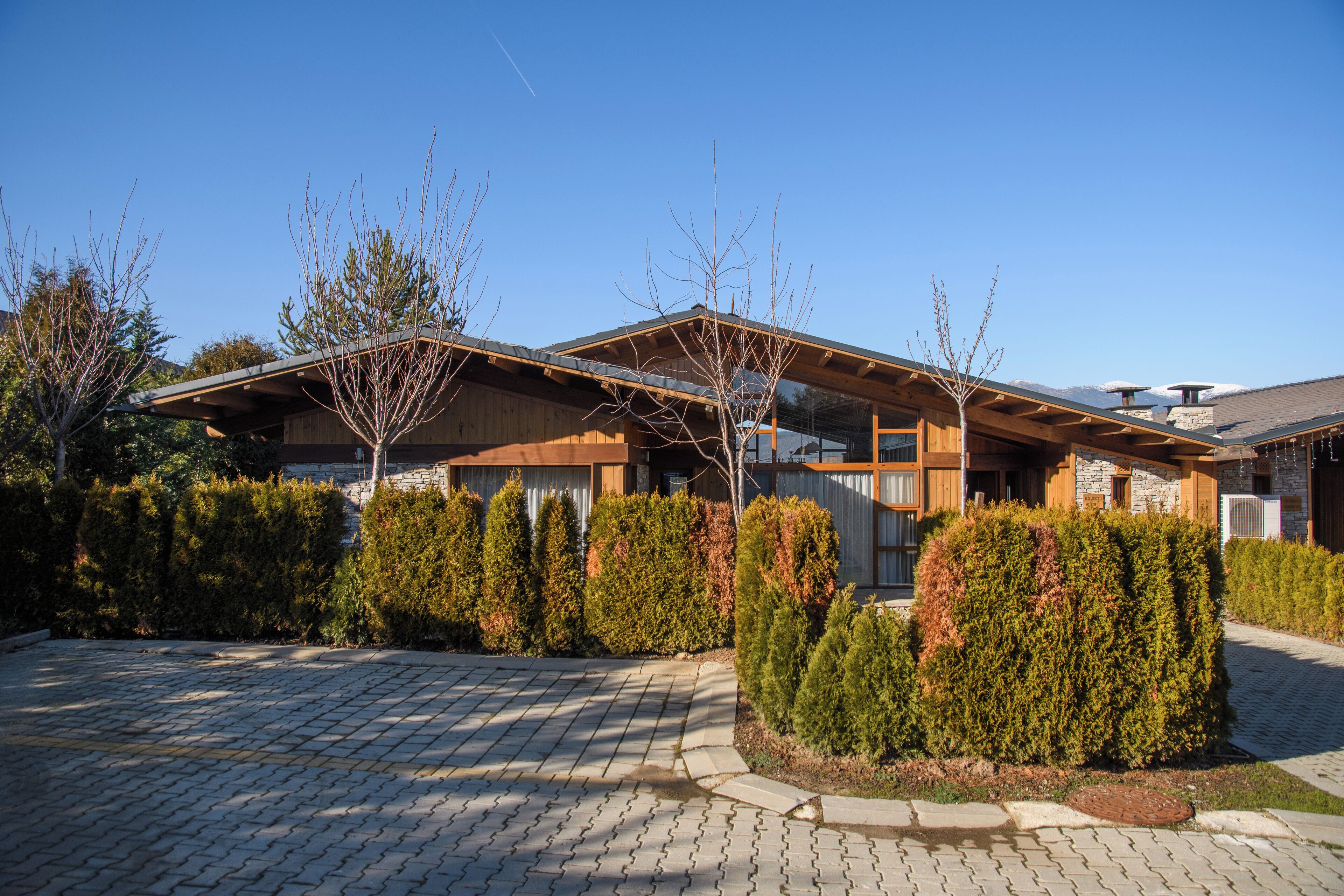 Ein modernes Haus mit Natursteinfassade, Holzbalken und einem gepflasterten Auffahrt.