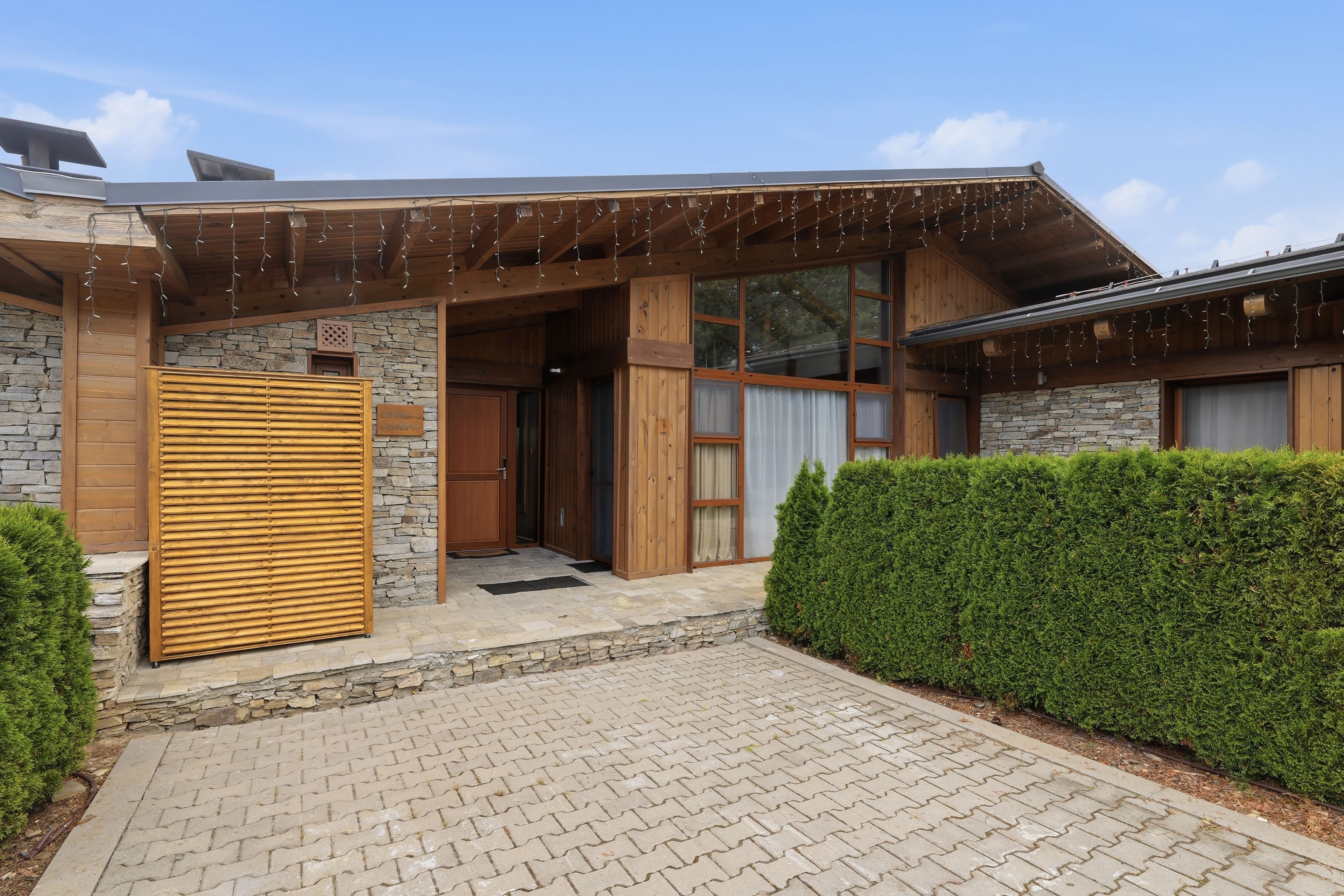 Ein modernes Haus mit Steinaußenwand, Holzklappen und einem gepflasterten Eingang.