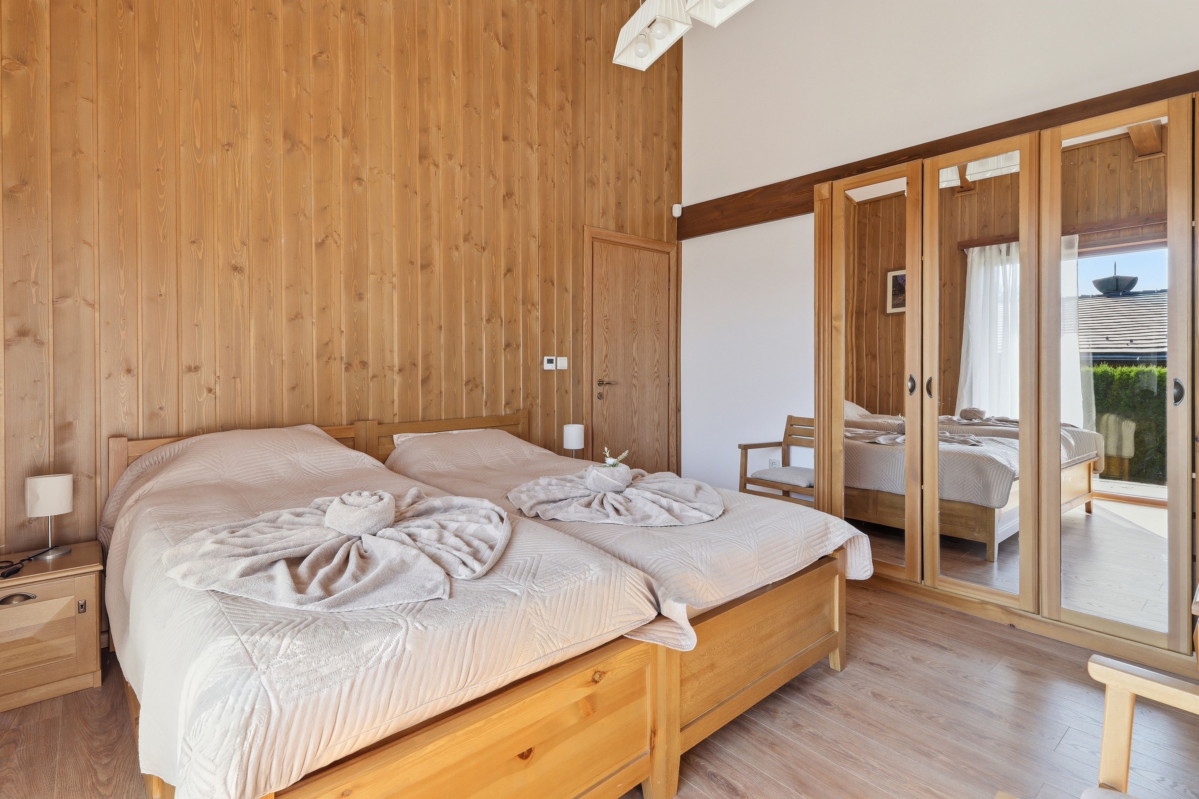 Een slaapkamer met houten vloer, een bed, nachtkastjes en uitzicht op een balkon.