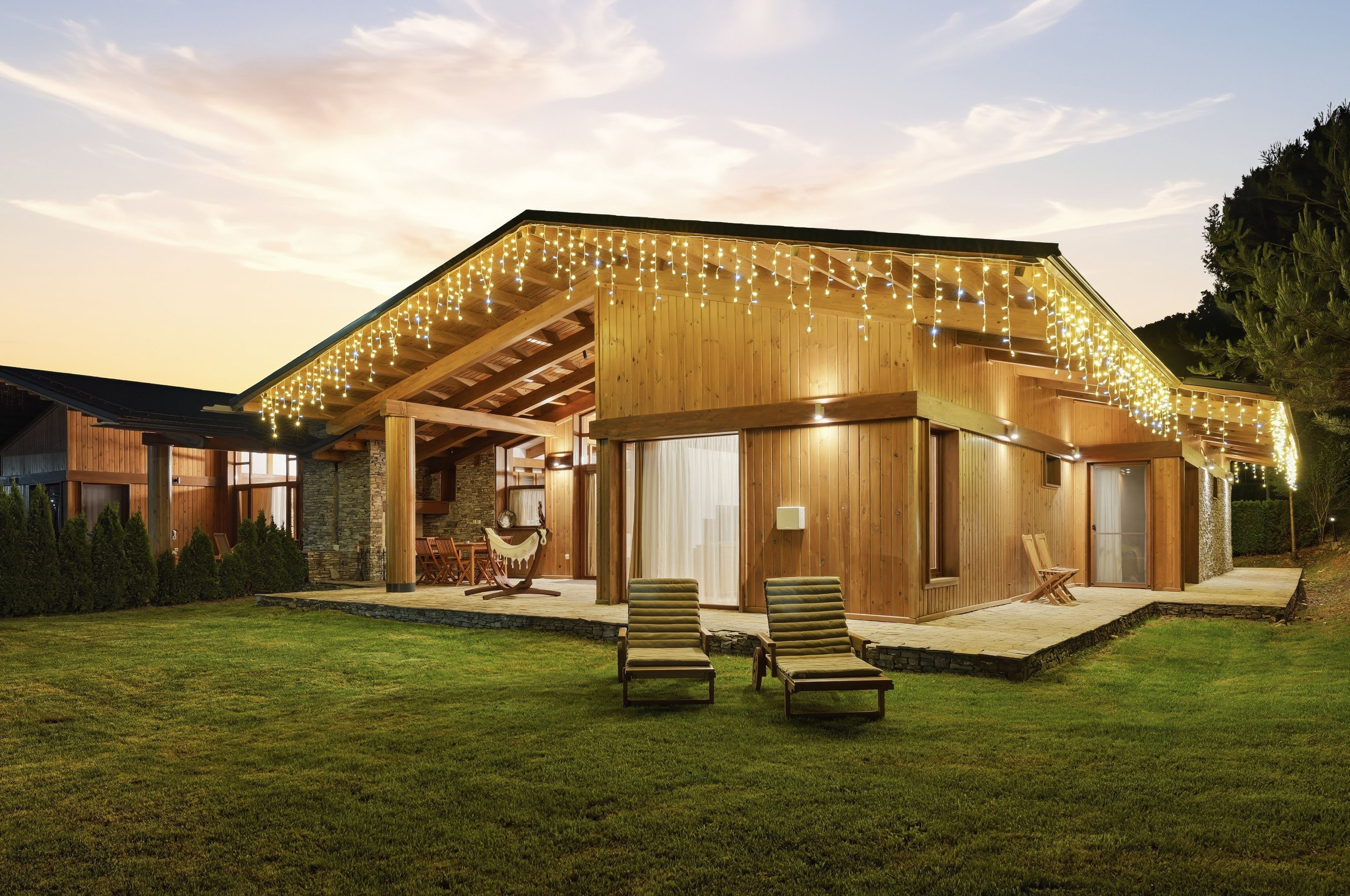 A modern wooden house with a covered patio, outdoor seating, and string lights.