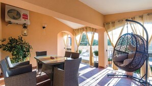 Eine sonnendurchflutete Terrasse mit Korbmöbeln, einem Hängesessel und Blick ins Freie.