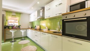 Eine moderne Küche mit weißen Schränken, einem schwarzen Backofen und einer grünen Spritzschutzwand. Zwei Barhocker und ein Fenster mit grünen Vorhängen sind ebenfalls vorhanden.