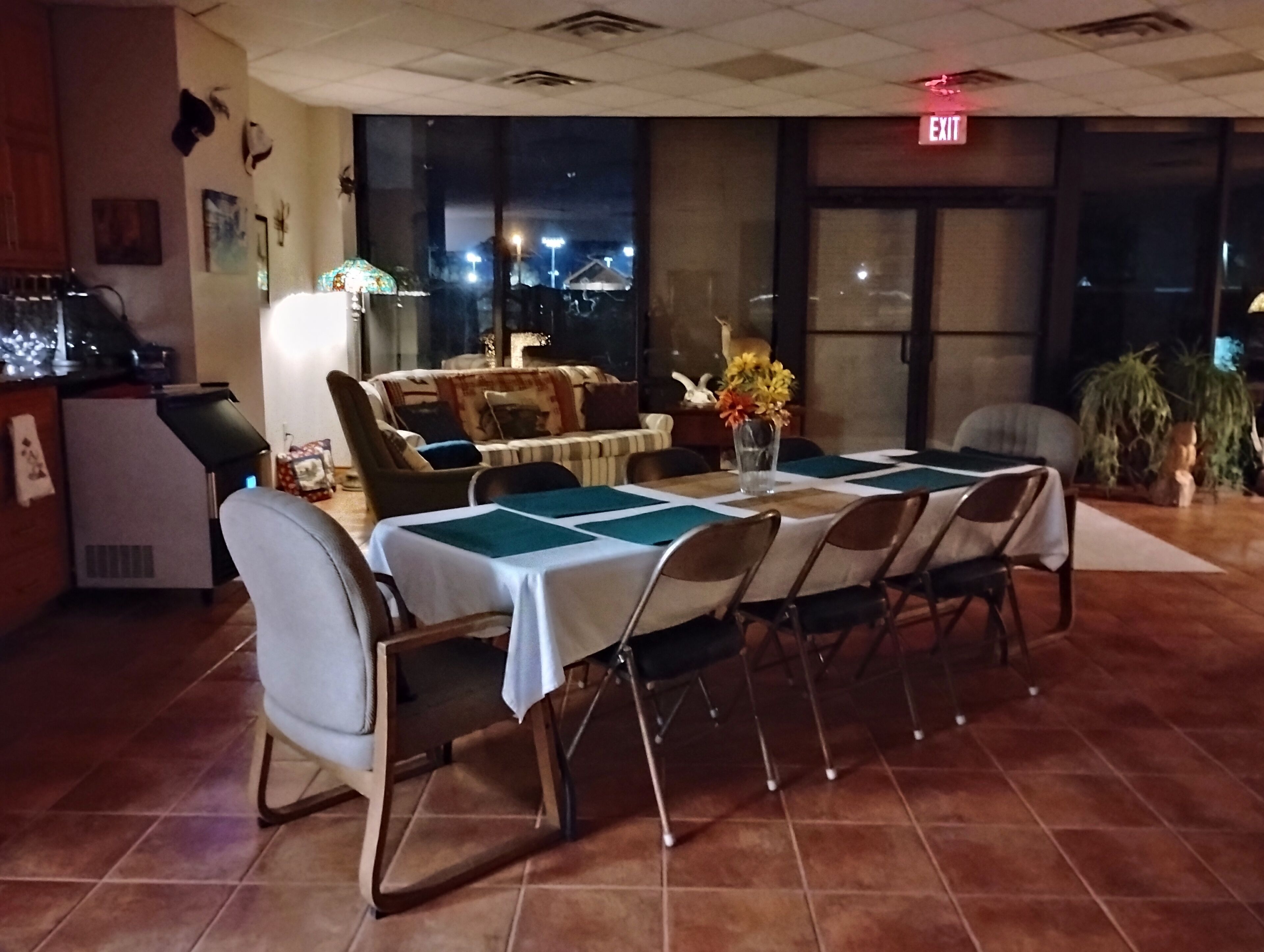 Comedor con mesa dispuesta para seis, sillas, un jarrón con flores y un sofá.