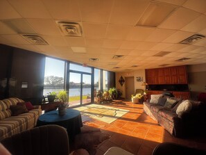 A spacious living room with a large window overlooking a body of water, a fireplace, and a kitchen area with wooden cabinets. - Waterfront 210’ dock boat launch 5 beds 2 bath. Great blue crab and fishing (Larose)