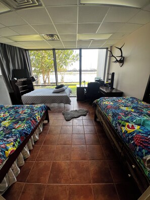 A hotel room with two beds, a desk, a chair, a TV, and a large window with a view of a body of water and greenery. - Waterfront 210’ dock boat launch 5 beds 2 bath. Great blue crab and fishing (Larose)
