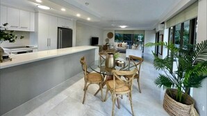 Une cuisine moderne avec des meubles blancs, un îlot central doté de sièges et une grande fenêtre offrant une vue sur l’extérieur.