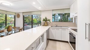 Une cuisine moderne avec des meubles blancs, un grand îlot central et une vue sur l’extérieur.