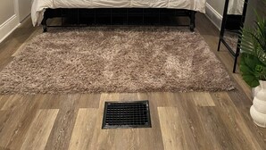 A bedroom with a sloped ceiling, a bed with a white bedspread, two bedside lamps, a window with blinds, a plant, and a radiator. - Stylish and comfortable! House close to downtown Akron. (Akron)