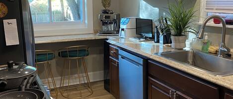 A modern kitchen with a stove, sink, and bar stools.