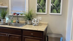 A kitchen with a granite countertop, stainless steel sink, and wooden cabinets. There are two potted plants on the counter and a trash can to the right. - Stylish and comfortable! House close to downtown Akron. (Akron)