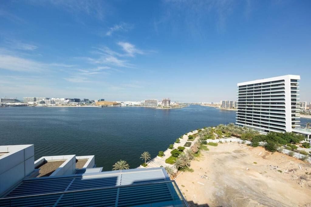 A high-rise hotel overlooking a body of water with a beach and palm trees in the foreground.